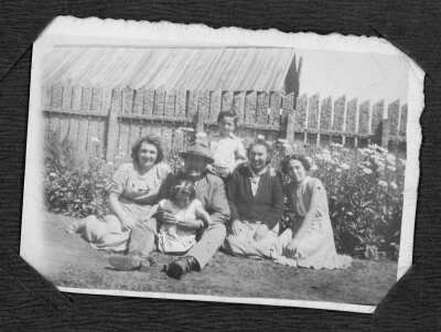 Retrato grupal de personas sentadas en el pasto, junto a un cerco de madera. Hay un hombre adulto, tres mujeres adultas, un niño y una niña.
