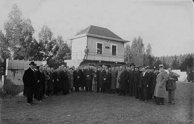 Retrato grupal de plano entero de Hombres y dos mujeres posando formados en media luna. La segunda mujer de izquierda a derecha es Olga Boettcher. Están ubicados en el exterior de un recinto no identificado, durante una convención de alcaldes realizada en La Unión