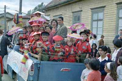 plano general de un grupo de niñas y Niños parados en la parte trasera de una camioneta, junto a Wilfred Casanova y Bella Uribe Jaramillo. Se puede observar que están disfrazados con un kimono rojo y sostienen una sombrilla durante un recorrido realizado en carros alegóricos por las calles de la Unión.