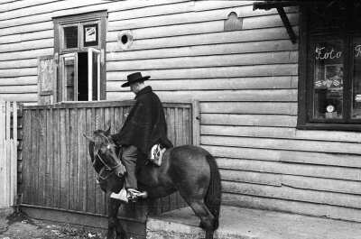 Retrato de plano general de un hombre posando montado en un caballo, el hombre lleva puesto una manta y sombrero, están en las afueras de un estudio fotográfico .