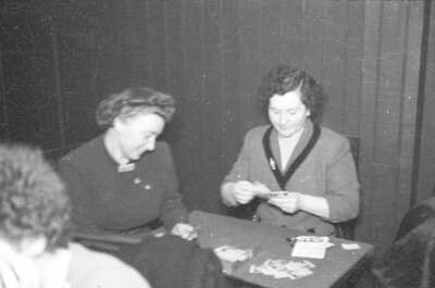 Plano entero de dos mujeres jugando al naipe sentadas en una mesa en el interior de un local