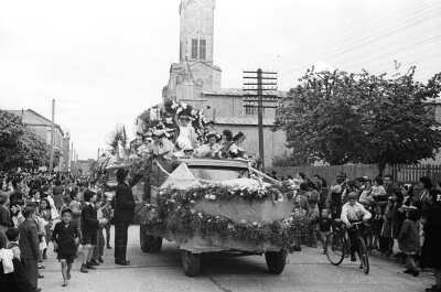 plano general de un grupo de Mujer junto a la reina en la parte trasera de un camión 43924 el cual va adornado con coronas de flores y guirnaldas. Las mujeres van saludando a un grupo de Niños y un hombre que las saludan desde un costado. Alrededor de la caravana, sobre la vereda, hay un grupo numeroso de Niños, Niñas, Mujer y Hombres observándolas durante el desfile realizado por las calles de La Unión