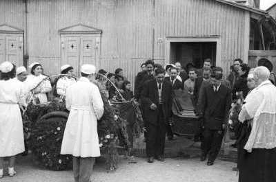 plano general de un grupo de hombres cargando un féretro desde el interior de una casa donde estaba siendo velado.