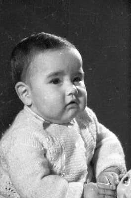 Retrato de estudio de Plano medio de Bebé de Medio perfil con chaleco de lana, sentado con una muñeca.