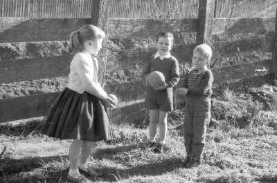 Plano entero de niña con Vestido y dos niños jugando con pelotas al lado de un cerco de madera