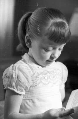 Plano medio de niña con blusa manga corta leyendo un libro