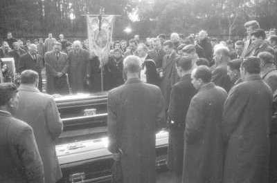 plano general de un grupo de Hombres y Mujeres reunidos junto a dos ataúdes mientras un sacerdote dirige el funeral, realizado en el interior del cementerio municipal de La Unión