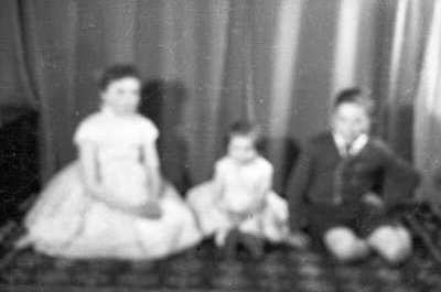 Retrato de estudio de Plano entero de dos niñas y un niño posando sentados sobre una alfombra. Fotografía borrosa