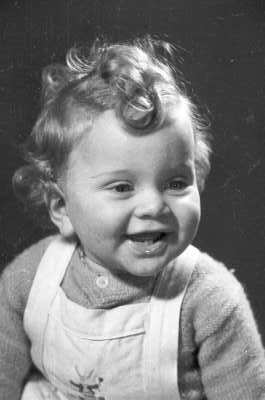 Retrato de estudio de Plano medio de una niña de temprana edad, sonriendo mientras posa de Medio perfil. Lleva puesta una jardinera