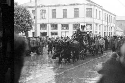 plano general de un cortejo fúnebre, caminando tras una carroza bajo la lluvia. Van caminando por un costado de la plaza de La Concordia