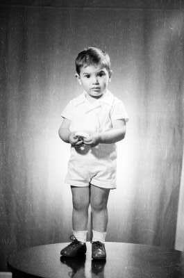 Retrato de estudio de Plano entero de un niño posando de frente con un objeto en las manos. Se encuentra parado sobre una mesa