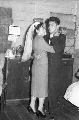 Plano entero de una pareja de recién casados bailando tomados de la mano, durante la celebración de su casamiento realizada en el interior de una casa