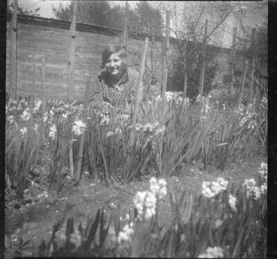 Plano medio de una mujer joven en cuclillas, posando entre las flores de un jardín