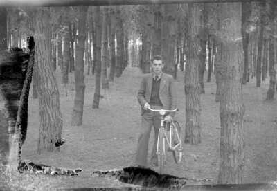 Plano general de un hombre joven posando de pie junto a una bicicleta en un entorno boscoso