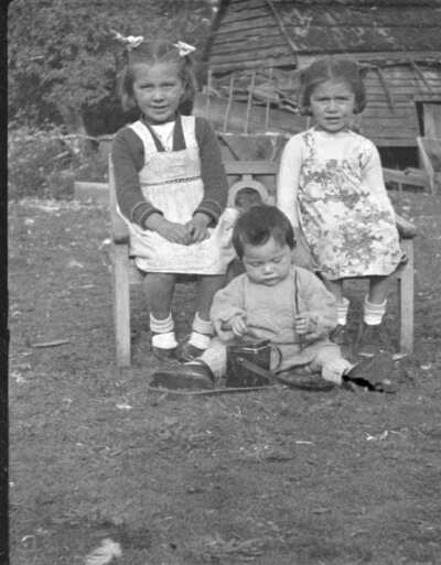 Plano entero de dos niñas pequeñas sentadas en una banca y un niño pequeño sentado en el suelo jugando con el estuche de una cámara fotográfica