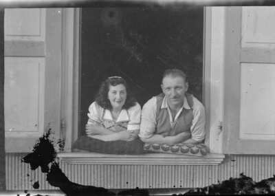 Plano general de un hombre y una mujer posando desde la ventada de un inmueble