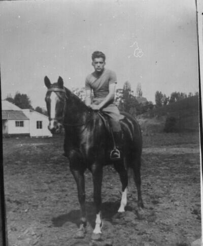 Reproducción de fotografía. Retrato de plano entero de Hombre montando un caballo, en un lugar no identificado